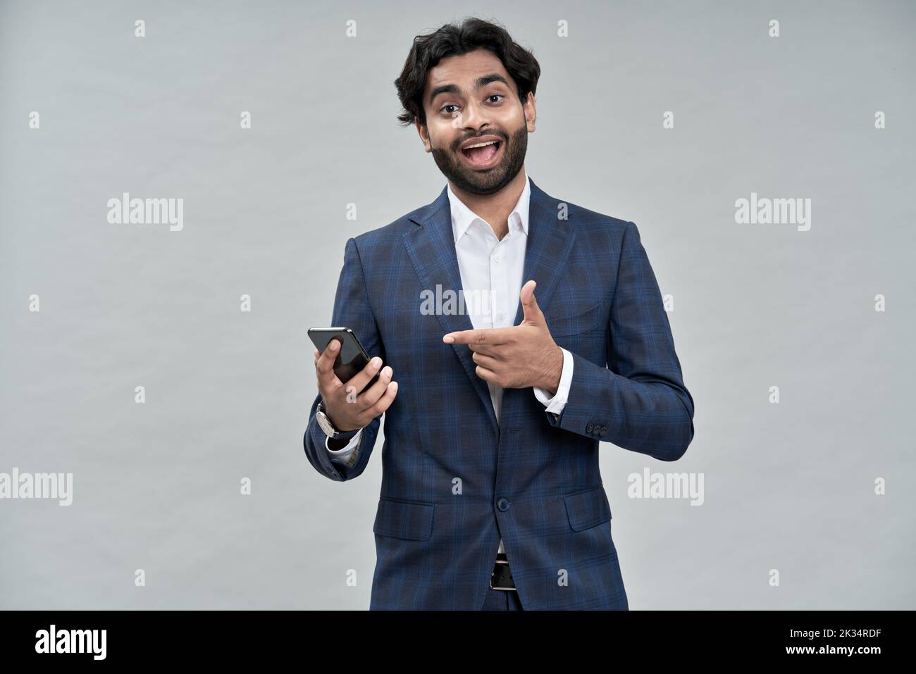 Entusiasmado hombre de negocios indio señalando a teléfono móvil aislado en beige. Foto de stock