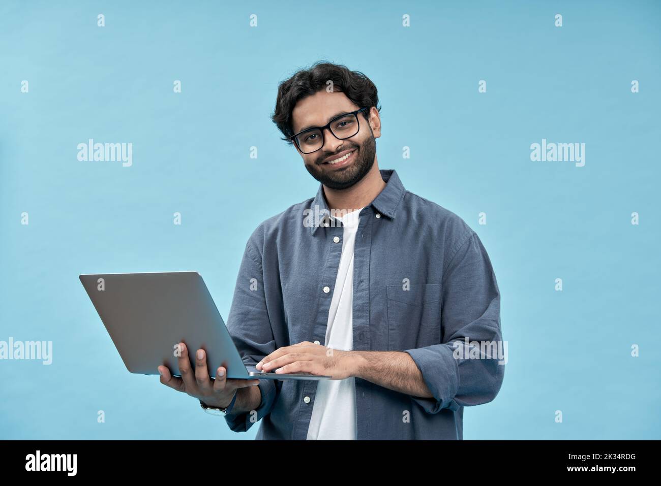 Feliz hombre de negocios árabe estudiante sosteniendo un portátil aislado en azul. Foto de stock