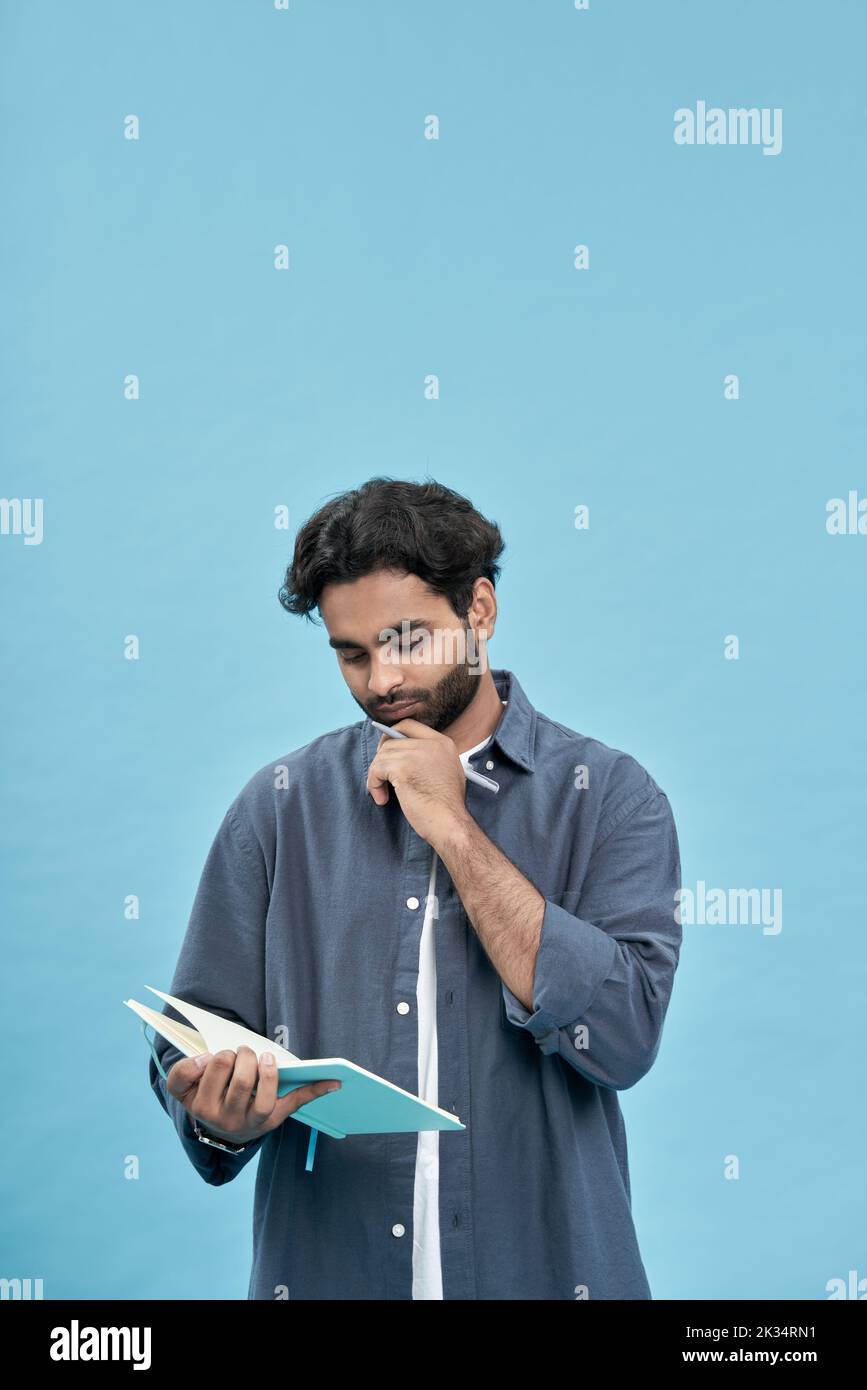 Pensativo joven árabe estudiante escribir en libreta aislado en azul. Foto de stock