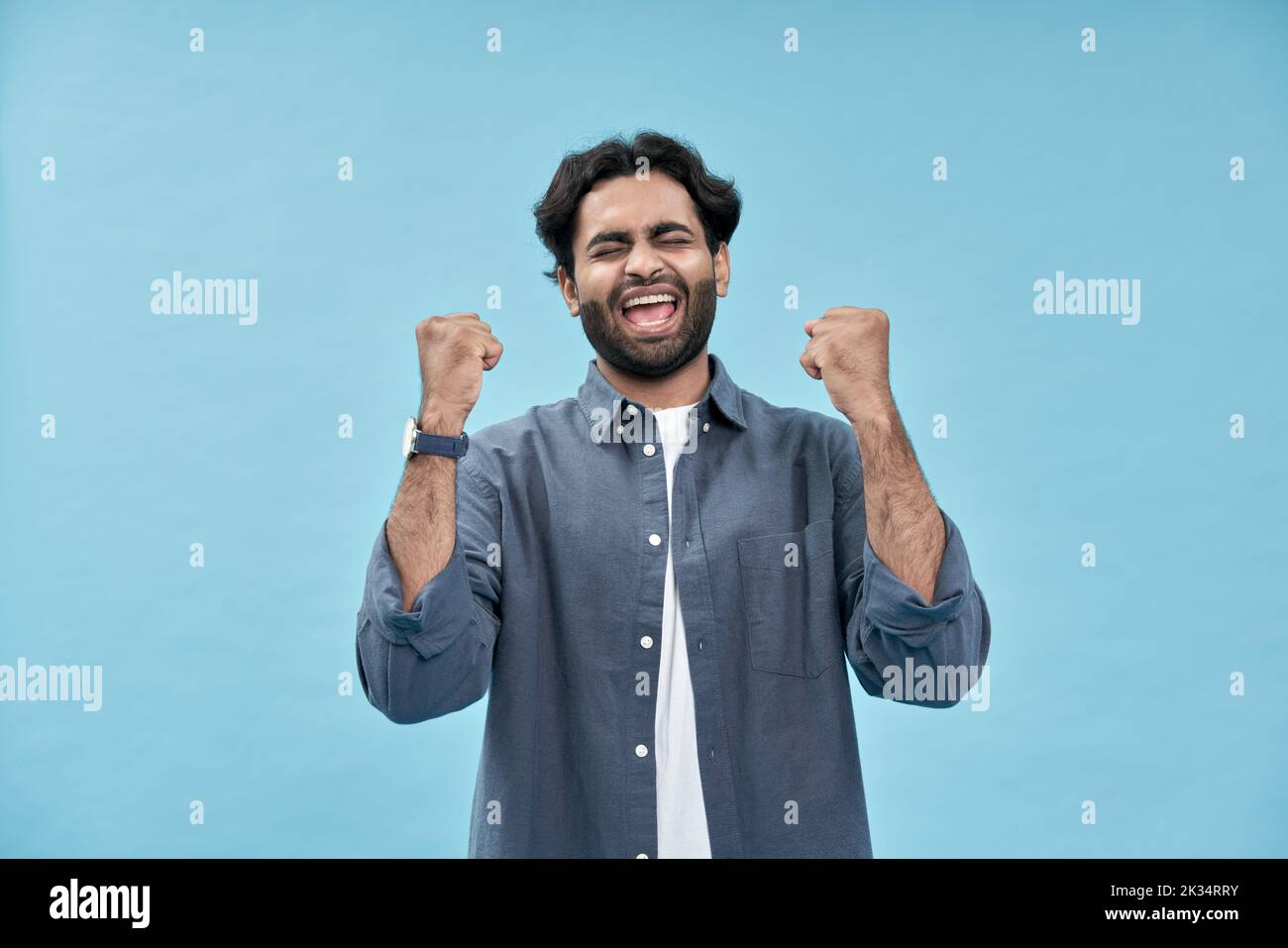 Feliz emocionado joven árabe levantando puños aislados sobre fondo azul. Foto de stock