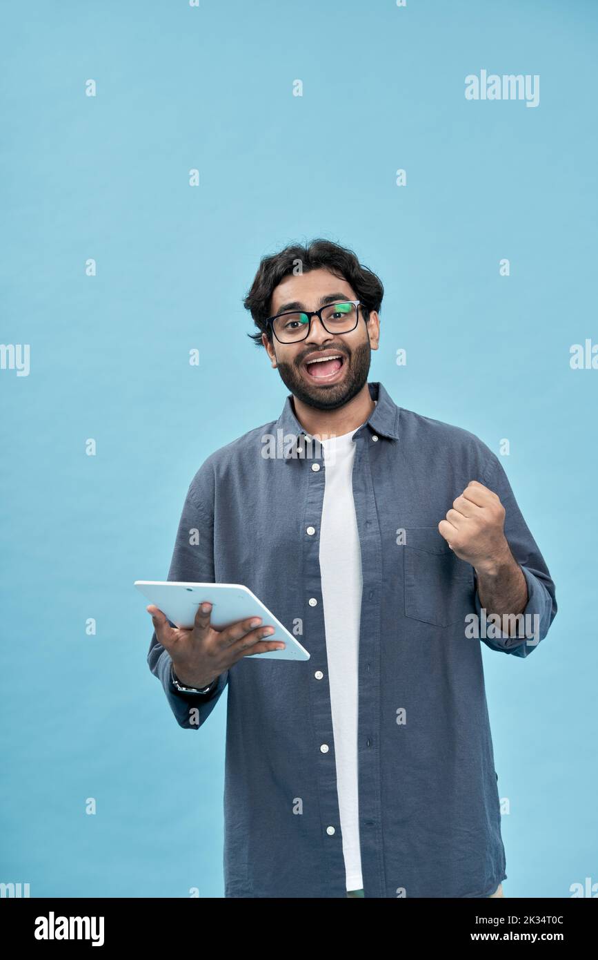 Ganador hombre árabe entusiasmado levantando la tableta fístulas aisladas en azul. Foto de stock