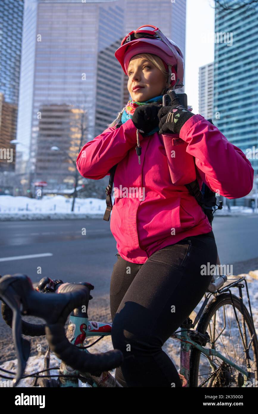 Mensajero para bicicleta mujer que coloca el smartphone en el bolsillo en la ciudad invernal Foto de stock