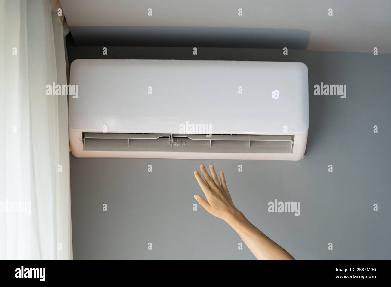 La mujer estira la mano para coger el flujo de aire e intenta calentar el apartamento para sentirse mejor Foto de stock