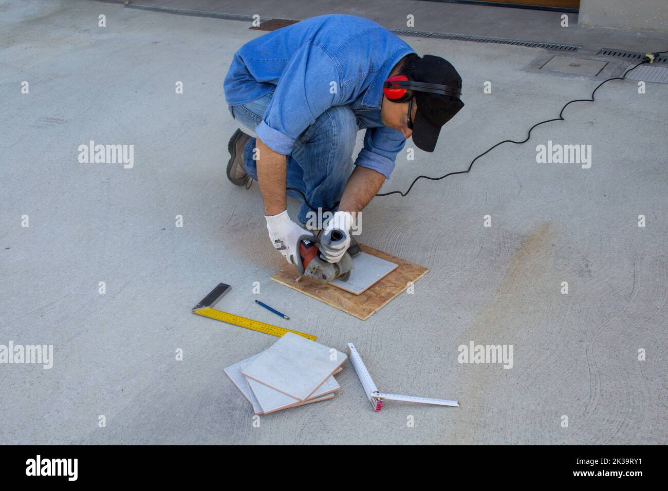 Imagen de un trabajador de la construcción cortando azulejos con una amoladora angular. Trabajo como un inclinador Foto de stock
