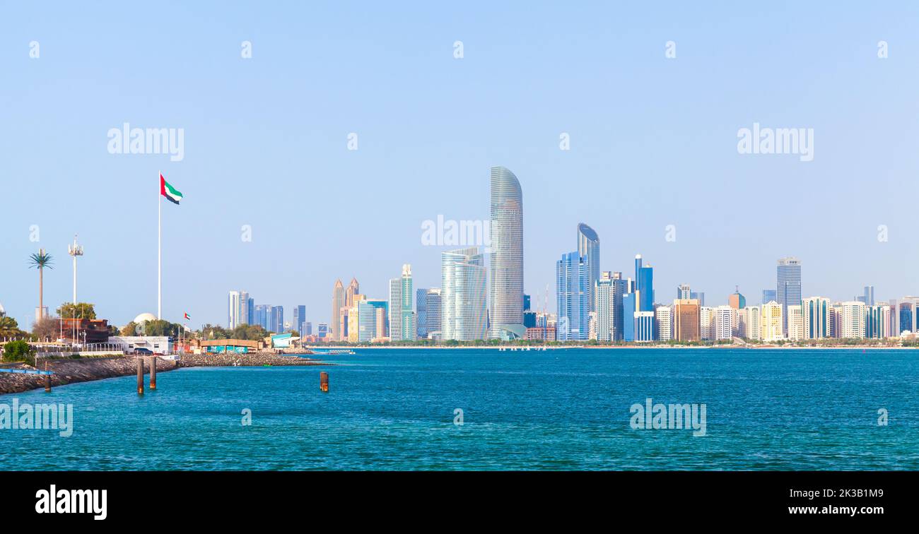 Abu Dhabi, Emiratos Árabes Unidos - 9 de abril de 2019: Paisaje urbano panorámico con rascacielos y bandera nacional de los Emiratos Árabes Unidos en la costa marítima Foto de stock