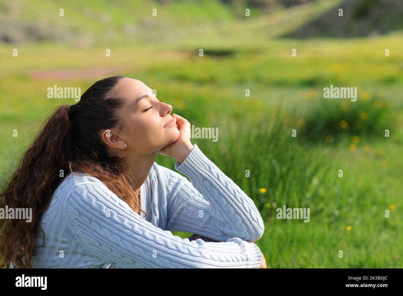 Mujer informal sentada en un campo verde en la montaña Foto de stock