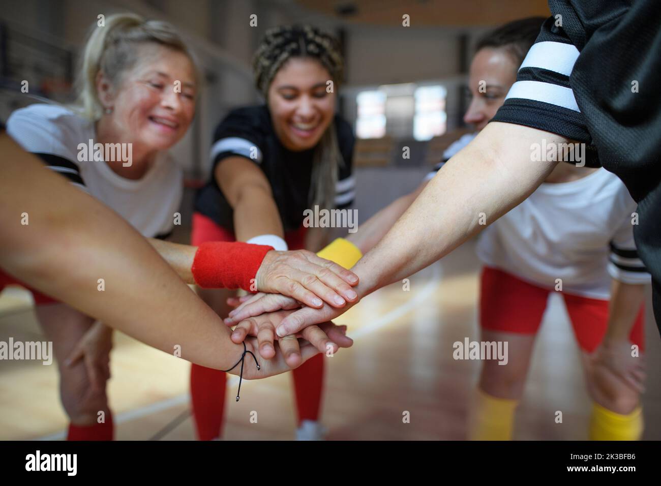 Grupo de mujeres jóvenes y mayores en el gimnasio apilando las manos juntas, jugadores de equipo deportivo. Foto de stock