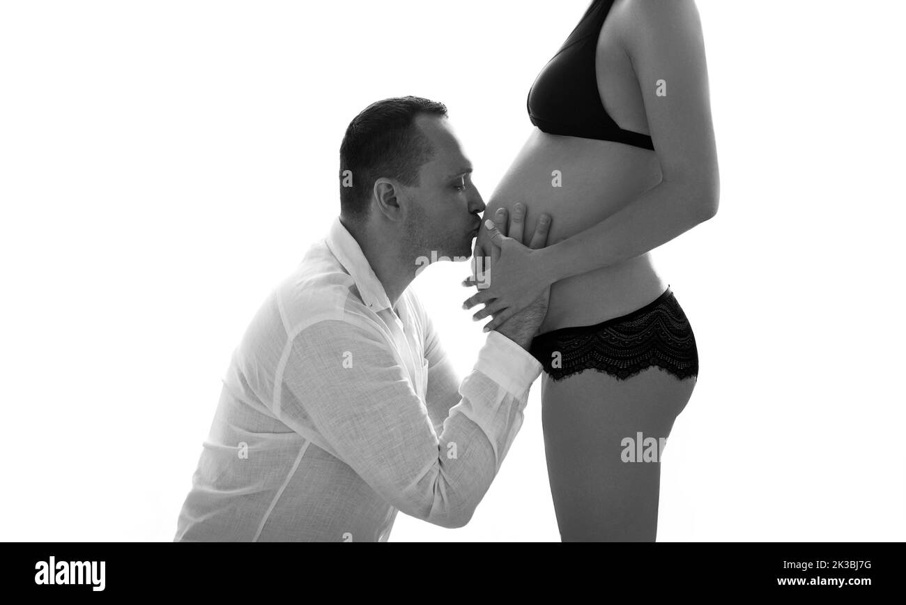 Hombre guapo besando el vientre mujer embarazada. Silueta retrato en blanco y negro. Feliz hermosa pareja embarazada. Marido tocando el estómago de la esposa yo Foto de stock