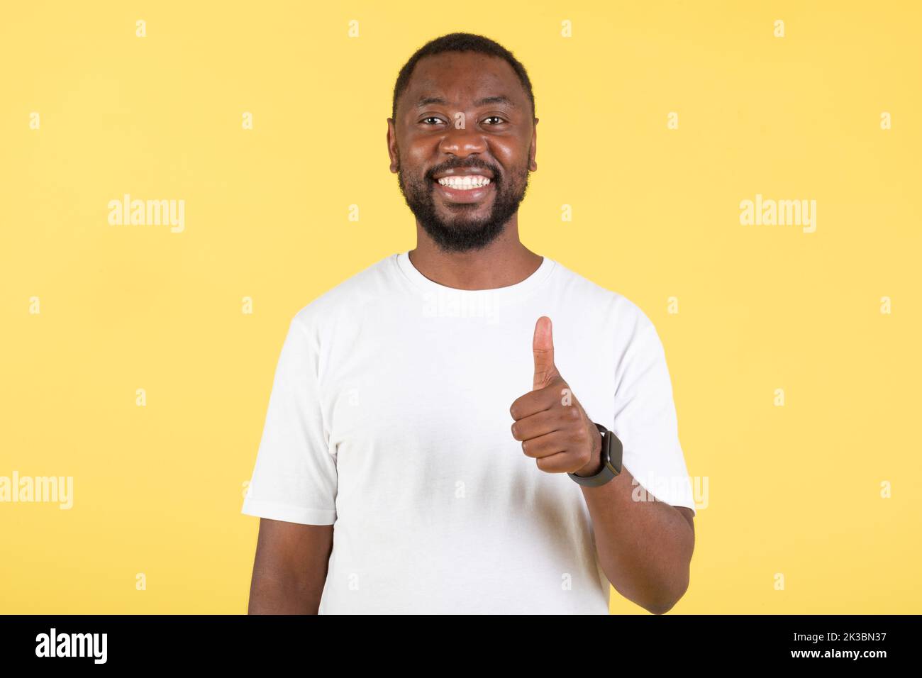 Feliz americano africano Guy Gestuuring Thumbs Up Posing, fondo amarillo Foto de stock
