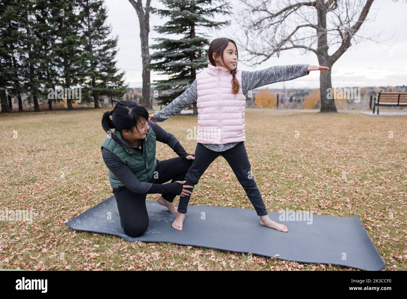 Madre ayudando a hija con yoga pose en el parque de otoño Foto de stock
