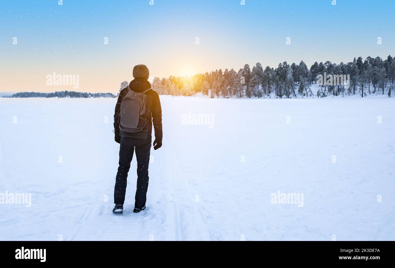 Hombre viajero con mochila caminando en la nieve disfrutando de la puesta de sol. Laponia, Finlandia. Foto de stock