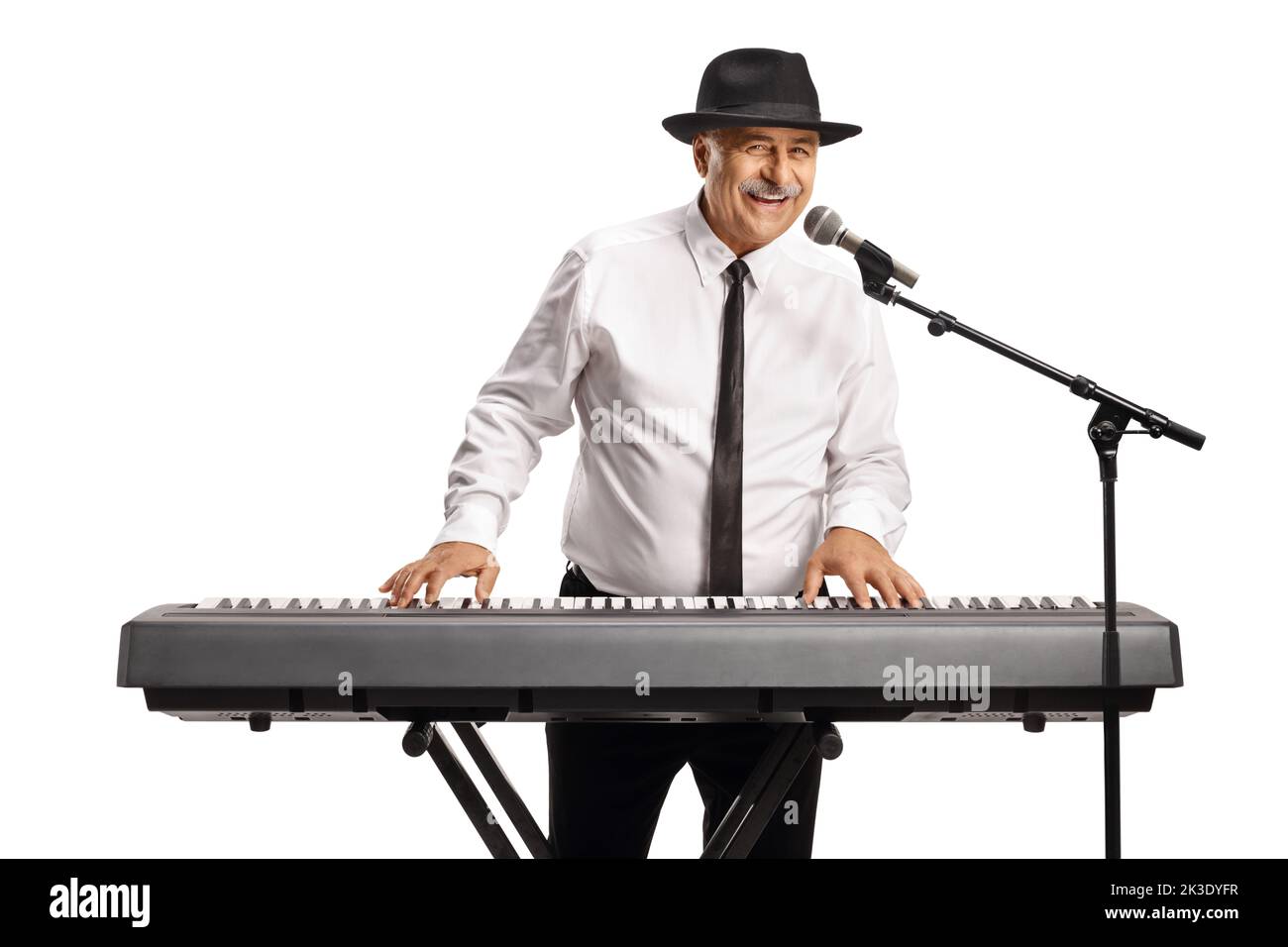 Hombre maduro alegre tocando un piano digital y cantando en un micrófono aislado sobre fondo blanco Foto de stock