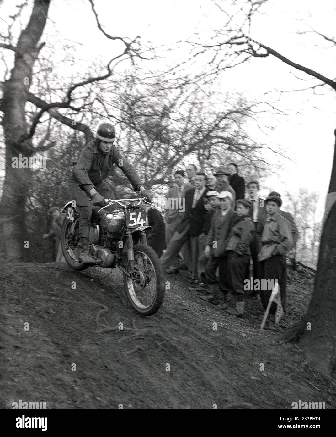 1954, histórico, en el exterior, en un terreno escarpado en un bosque, espectadores viendo a un competidor montando una motocicleta de la época, en una carrera de lucha o prueba en Seacroft, Leeds, Inglaterra, Reino Unido, organizada por el West Leeds Motor Club. Foto de stock