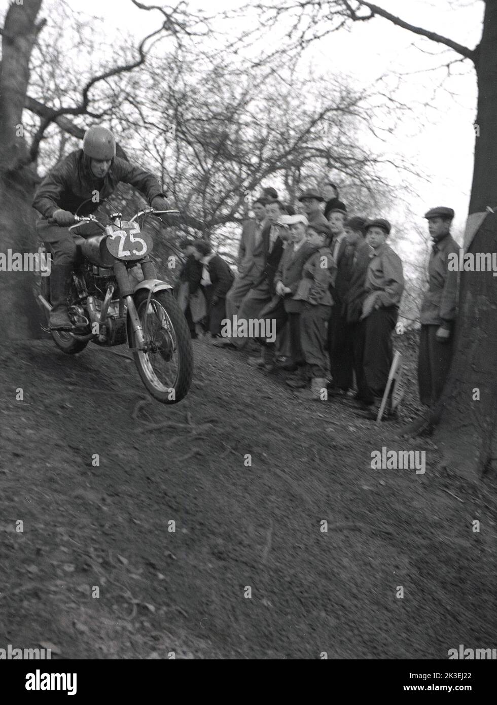 1954, histórico, en el exterior, en un terreno escarpado en un bosque, espectadores viendo a un competidor montando una motocicleta de la época, en una carrera de lucha o prueba en Seacroft, Leeds, Inglaterra, Reino Unido, organizada por el West Leeds Motor Club. Foto de stock