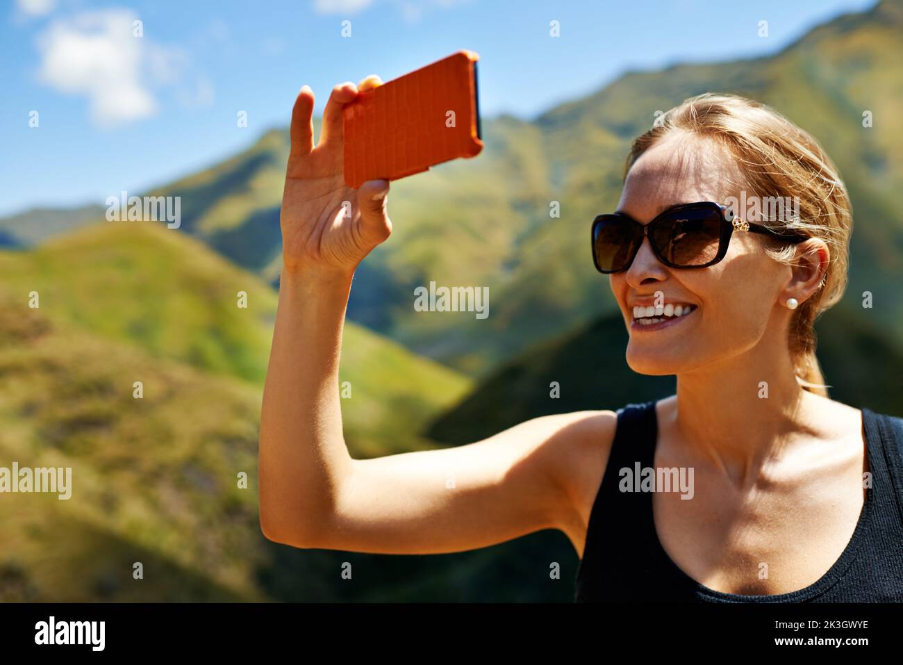 Capturar recuerdos de montaña. Una mujer joven tomando una fotografía en la ladera de la montaña. Foto de stock
