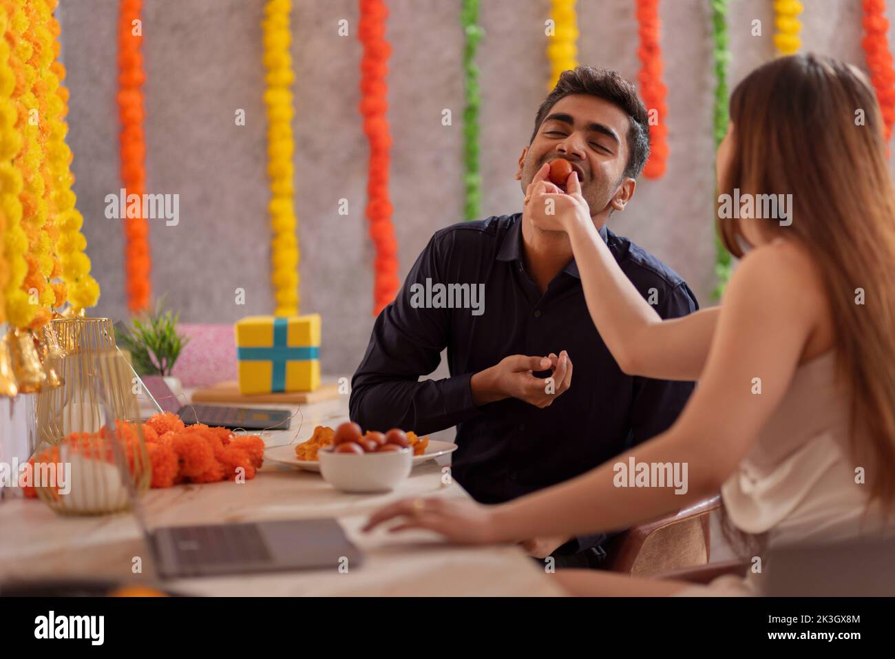 Una empleada que da de comer dulce a su colega en la oficina durante la celebración de Diwali Foto de stock