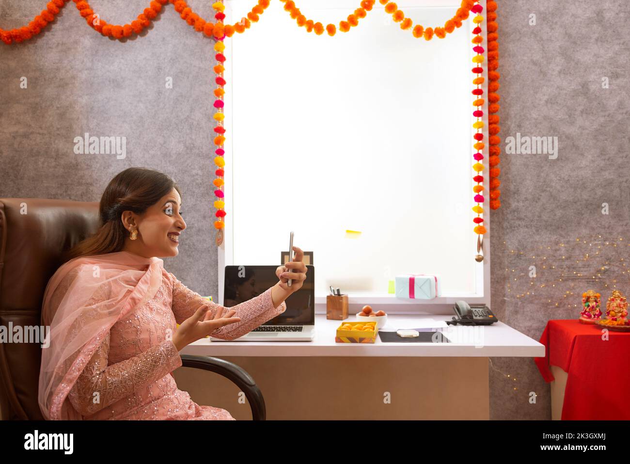 Mujer haciendo videollamada en el teléfono móvil en la oficina durante la celebración de Diwali Foto de stock