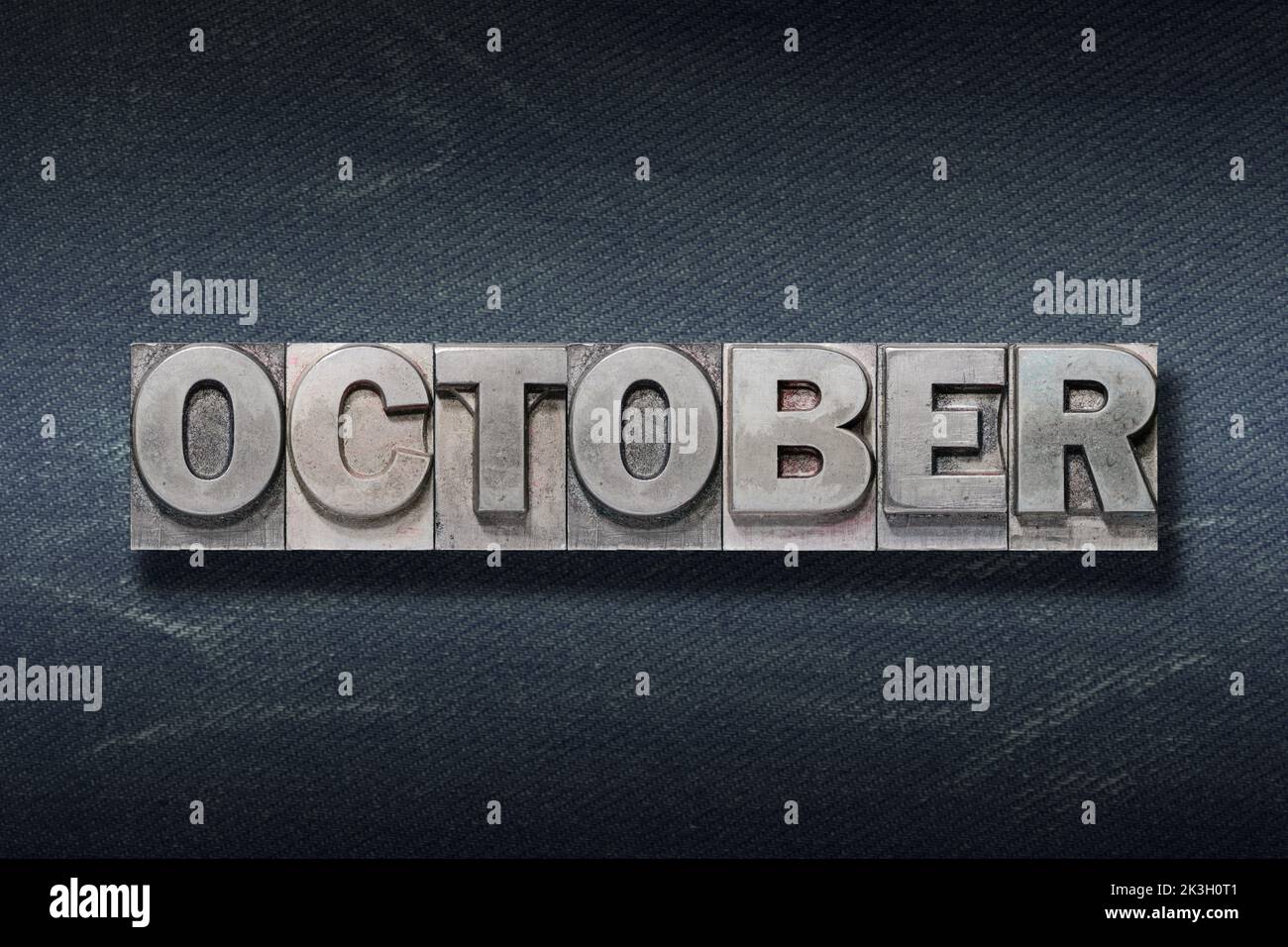 Palabra de octubre hecha de letterpress metálico sobre fondo de vaqueros oscuros Foto de stock