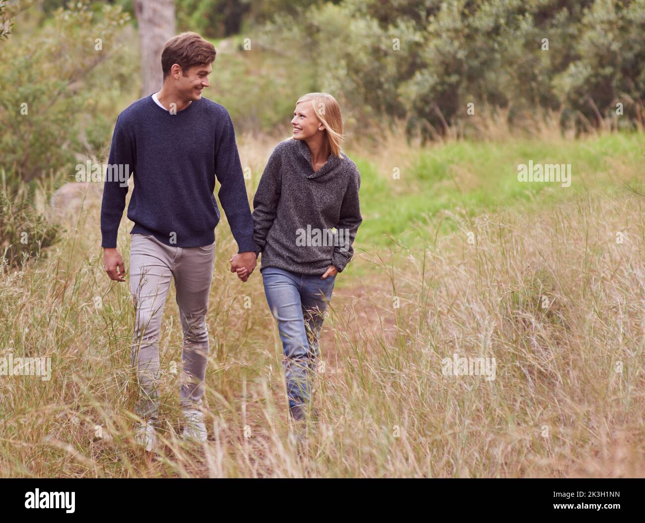 Paseo romántico por el campo. Una joven pareja paseando mano en mano a través de un prado. Foto de stock
