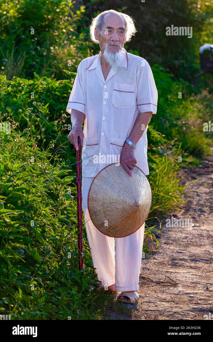Viejo vietnamita con pelo blanco, barba y sombrero de bambú al lado de la carretera, rural Hai Phong, Vietnam Foto de stock