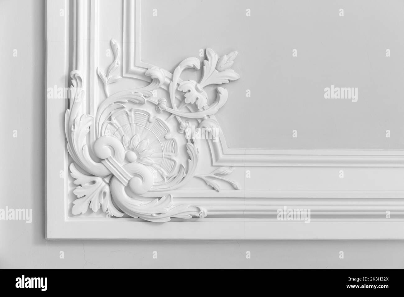 Pared blanca con decoración clásica de estuco, fragmento interior abstracto con patrón floral en una esquina Foto de stock
