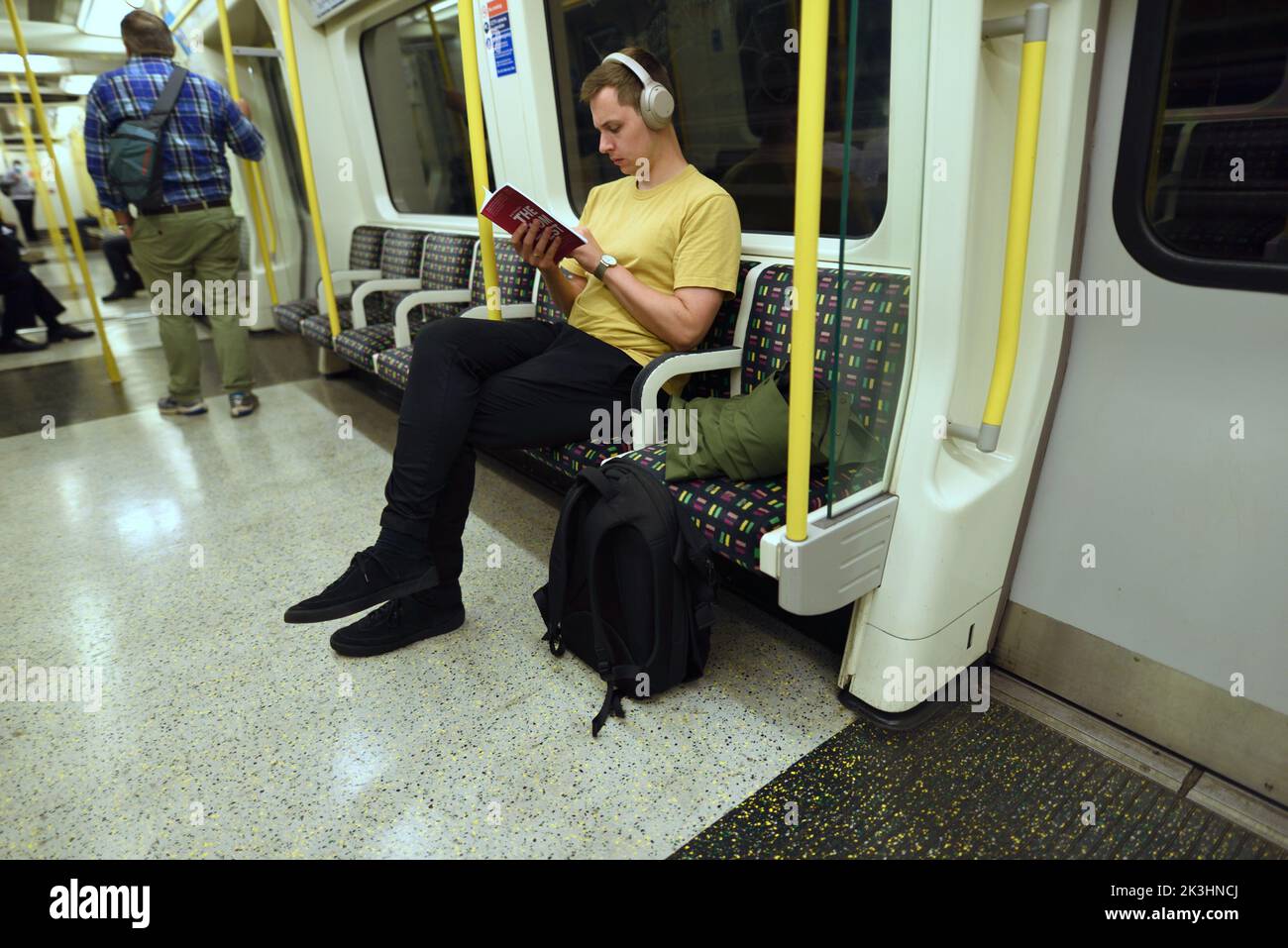 Londres, Inglaterra, Reino Unido. Hombre leyendo un libro en el tubo, usando auriculares Foto de stock