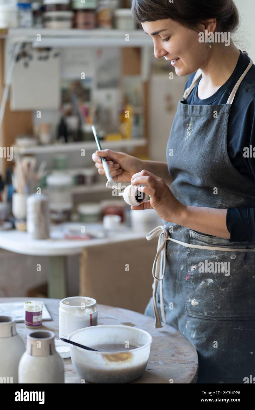 A la joven ceramista le gusta hacer y pintar productos hechos a mano de arcilla en el taller. Foto de stock
