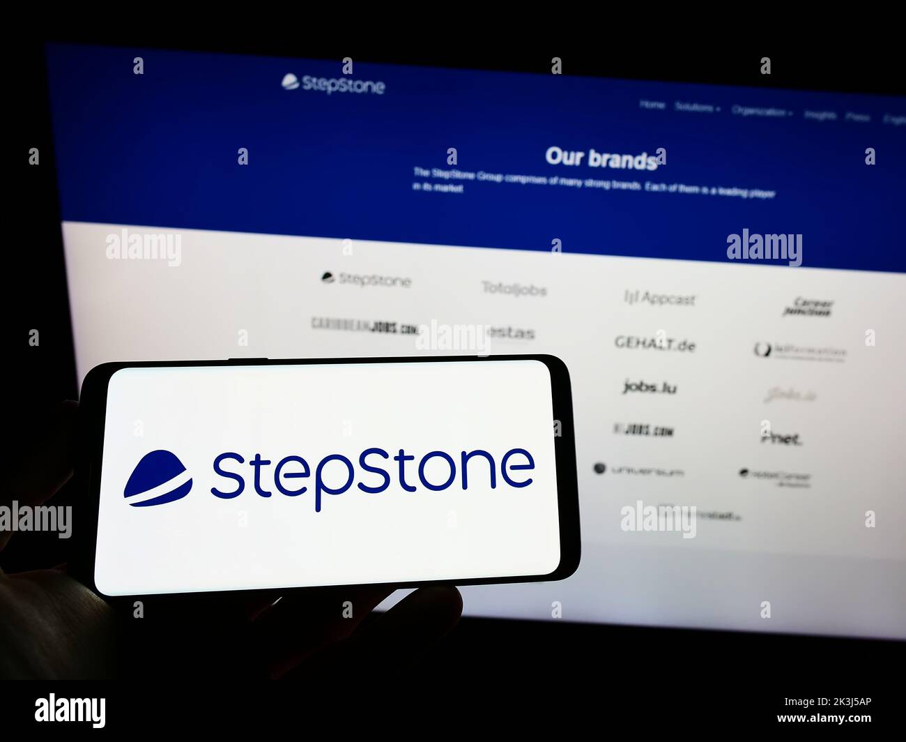 Persona que sostiene el teléfono móvil con el logotipo de la empresa alemana de empleo StepStone GmbH en la pantalla delante de la página web de negocios. Enfoque la pantalla del teléfono. Foto de stock