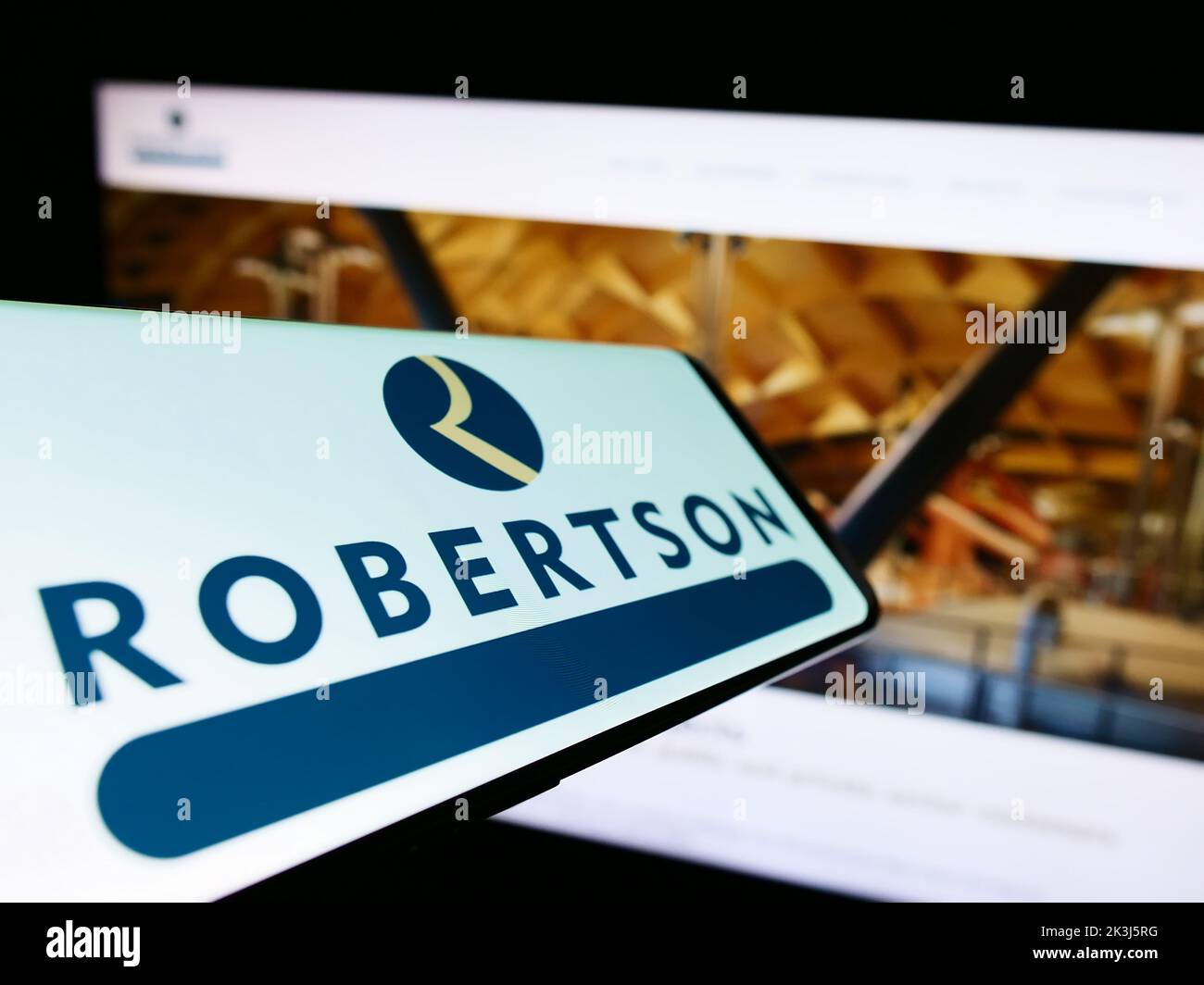 Teléfono móvil con el logotipo de la empresa de construcción Robertson Group Limited en la pantalla frente a la página web del negocio. Enfoque en el centro de la pantalla del teléfono. Foto de stock