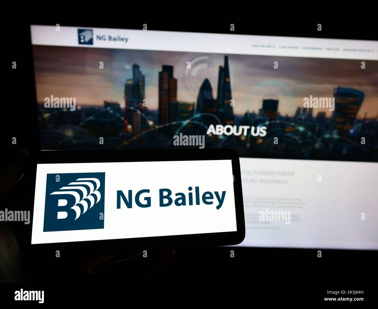 Persona que sostiene el smartphone con el logotipo de la empresa de ingeniería NG Bailey Group Limited en la pantalla delante del sitio web. Enfoque la pantalla del teléfono. Foto de stock