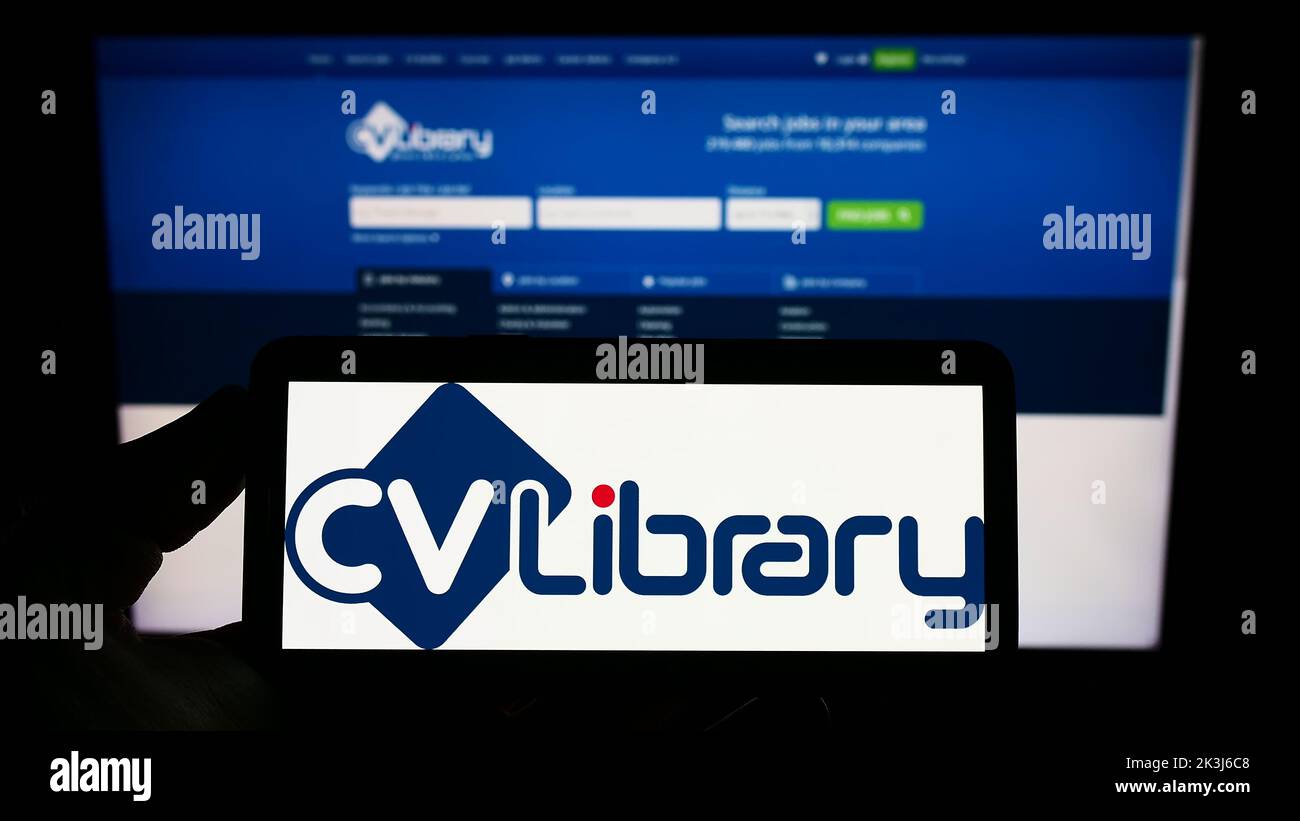 Persona que sostiene el smartphone con el logotipo de la compañía británica del tablero de trabajo CV-Library Ltd. En la pantalla delante del Web site. Enfoque la pantalla del teléfono. Foto de stock