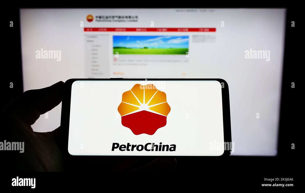 Persona que sostiene el teléfono celular con el logotipo de la compañía china de petróleo y gas PetroChina Company Limited en la pantalla delante de la página web. Enfoque la pantalla del teléfono. Foto de stock