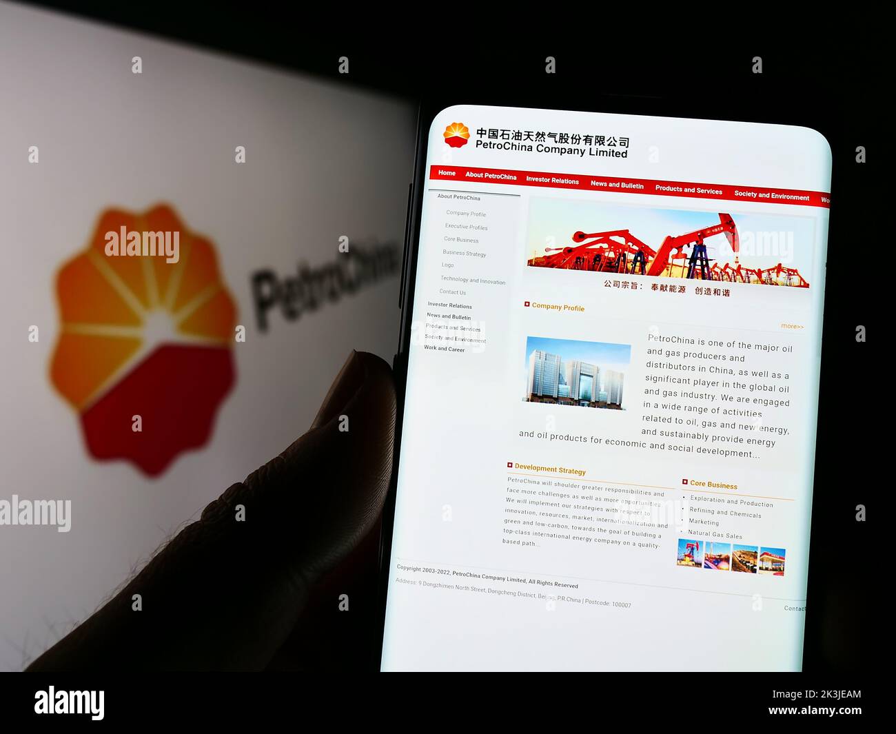 Persona que sostiene el teléfono celular con el Web site del petróleo y del gas chino PetroChina Company Limited en la pantalla con el logotipo. Enfoque en el centro de la pantalla del teléfono. Foto de stock