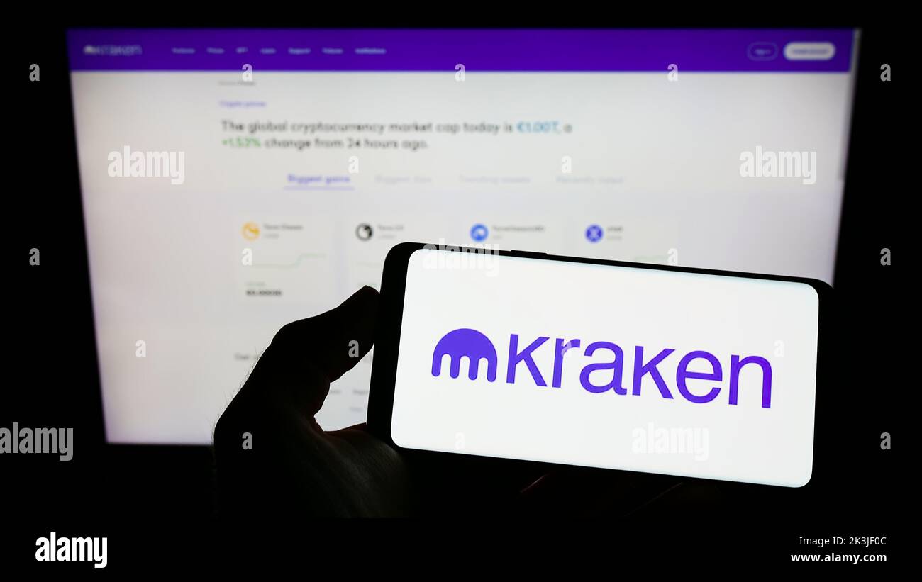 Persona que sostiene un smartphone con el logotipo de la empresa estadounidense Payward Inc. (Kraken) en la pantalla delante del sitio web. Enfoque la pantalla del teléfono. Foto de stock
