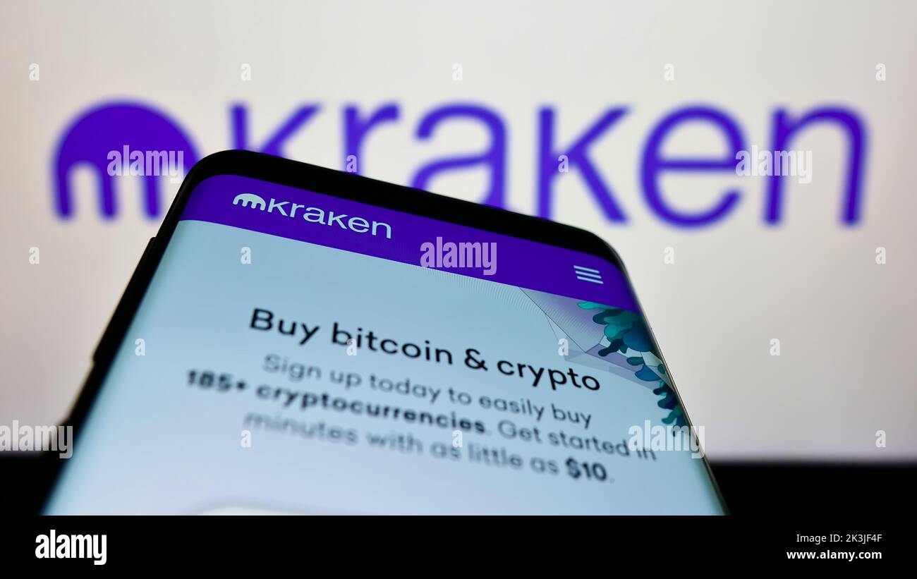Smartphone con sitio web de la empresa estadounidense Payward Inc. (Kraken) en pantalla delante del logotipo de la empresa. Enfoque en la parte superior izquierda de la pantalla del teléfono. Foto de stock