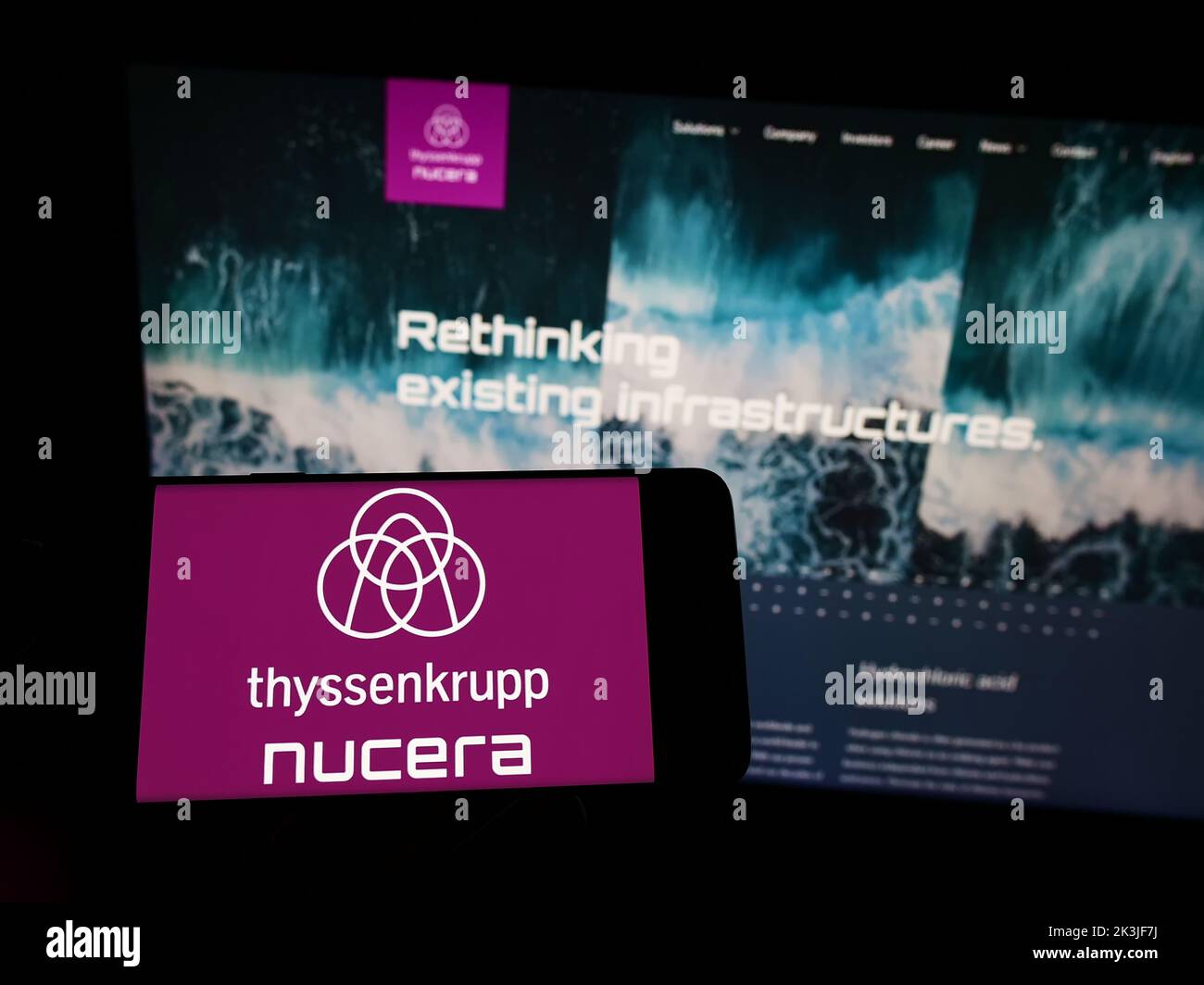 Persona que sostiene el teléfono celular con el logotipo de la empresa thyssenkrupp nucera AG Co. KGaA en la pantalla frente a la página web del negocio. Enfoque la pantalla del teléfono. Foto de stock
