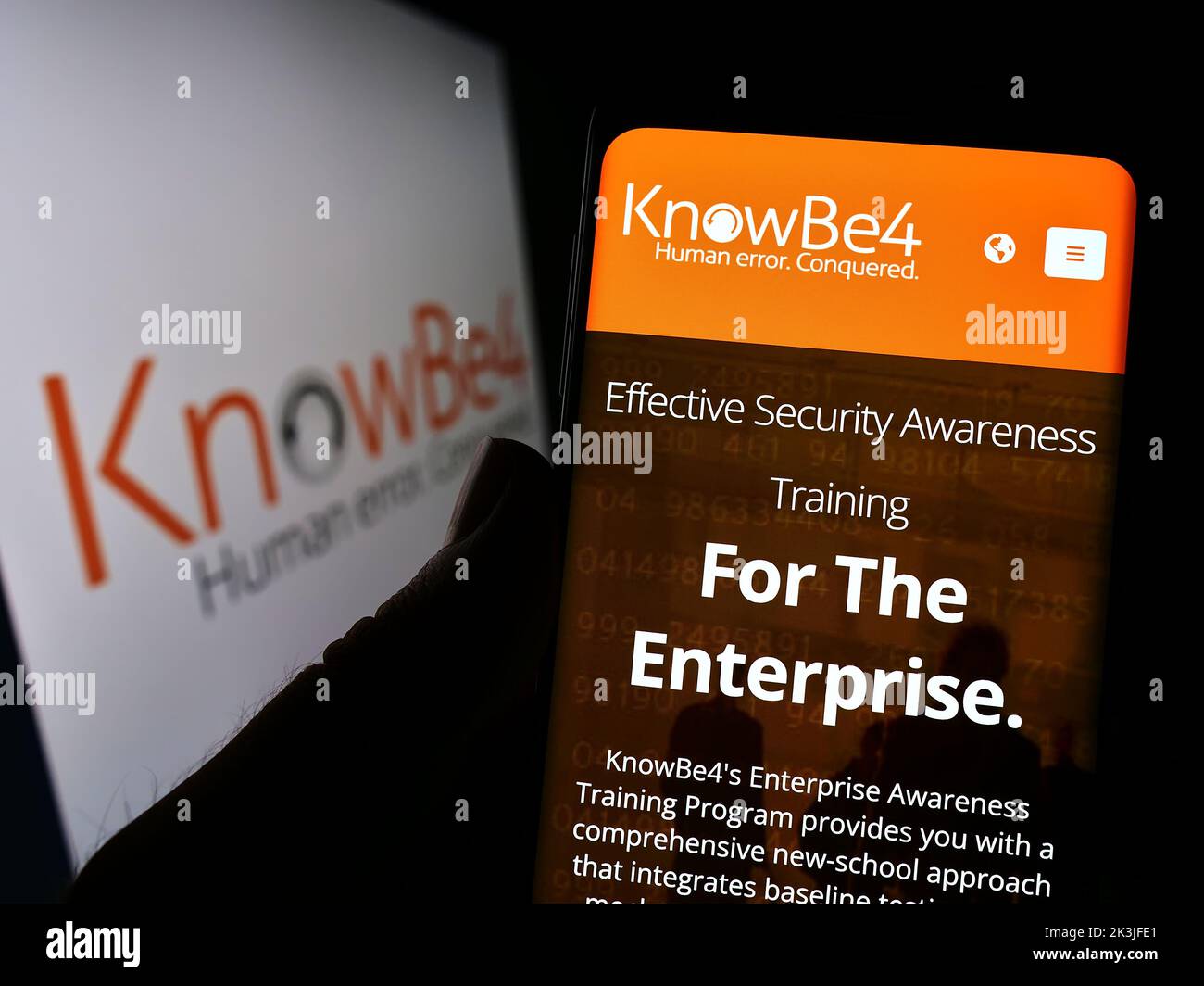 Persona que sostiene el teléfono móvil con el Web site de la compañía KnowBe4 inc. Del conocimiento de la seguridad de los E.E.U.U. en la pantalla con el logotipo. Enfoque en el centro de la pantalla del teléfono. Foto de stock