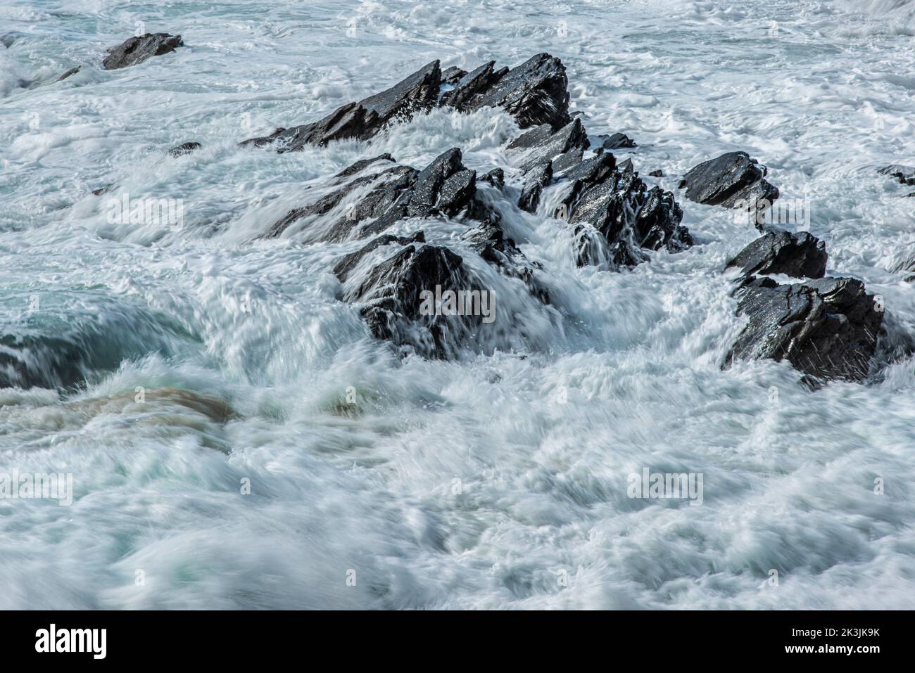 La marea entrante fluye sobre rocas irregulares en Fistral Bay en Newquay, en Cornwall, Reino Unido. Foto de stock
