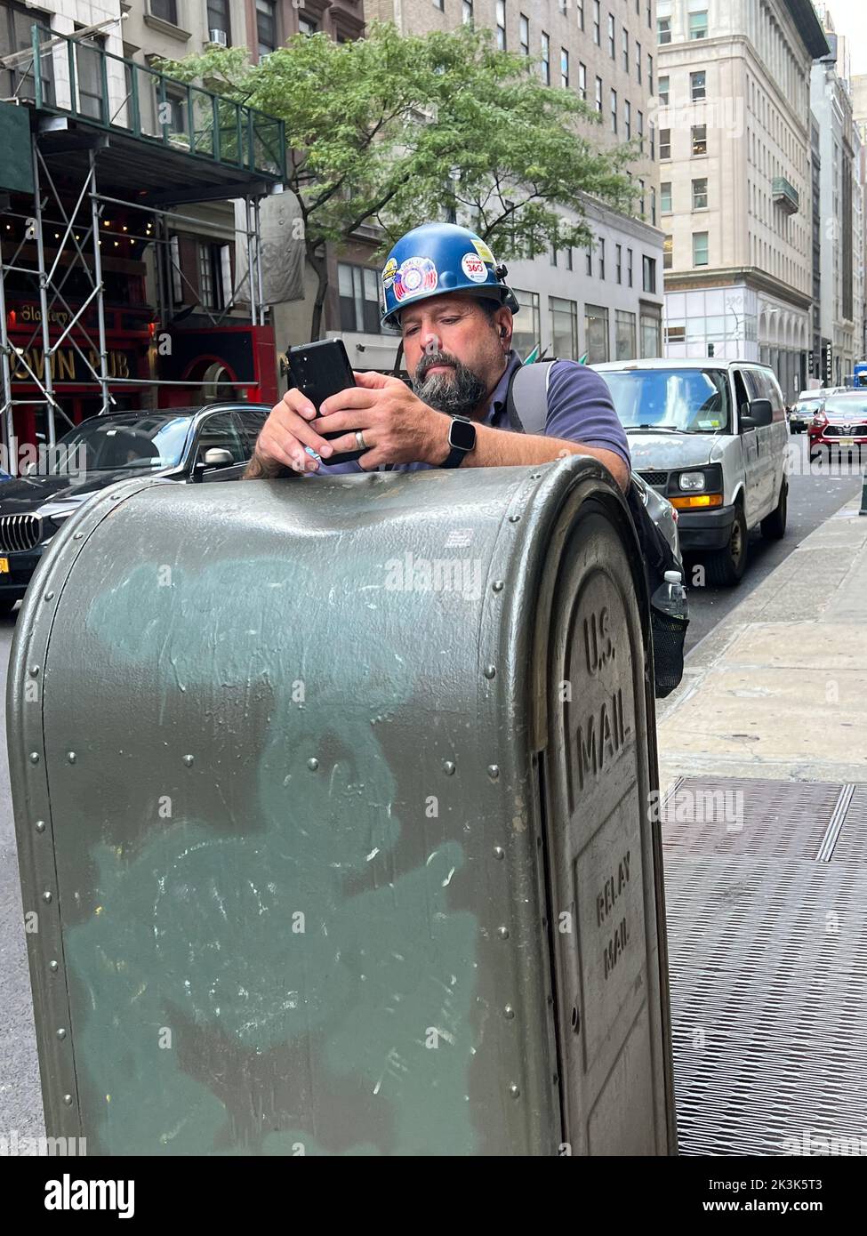 Trabajador de la construcción en su teléfono en la acera durante un descanso. Manhattan, Nueva York. Foto de stock