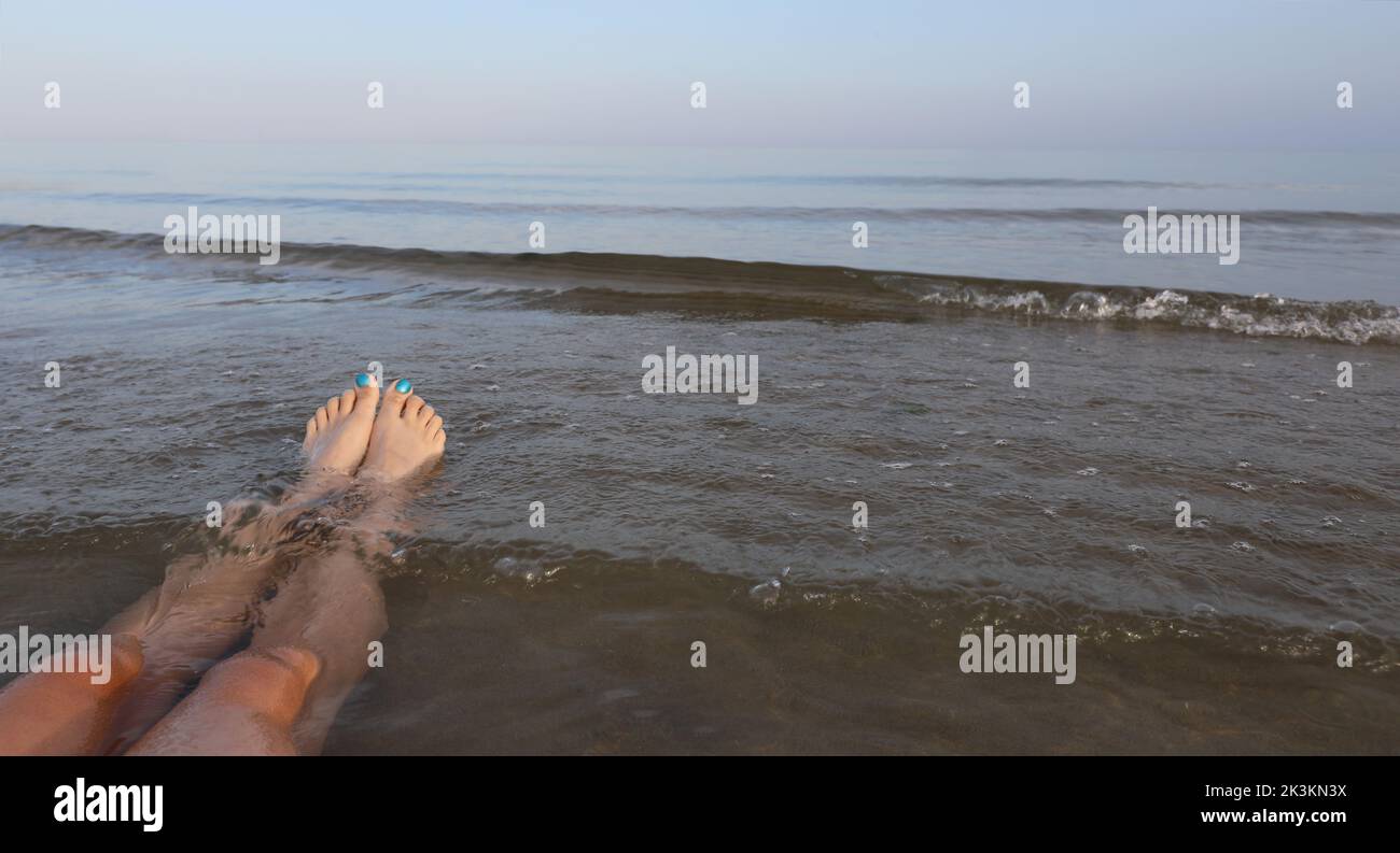 patas largas con uñas de los pies esmaltadas mientras se relaja en el agua del mar en el verano Foto de stock