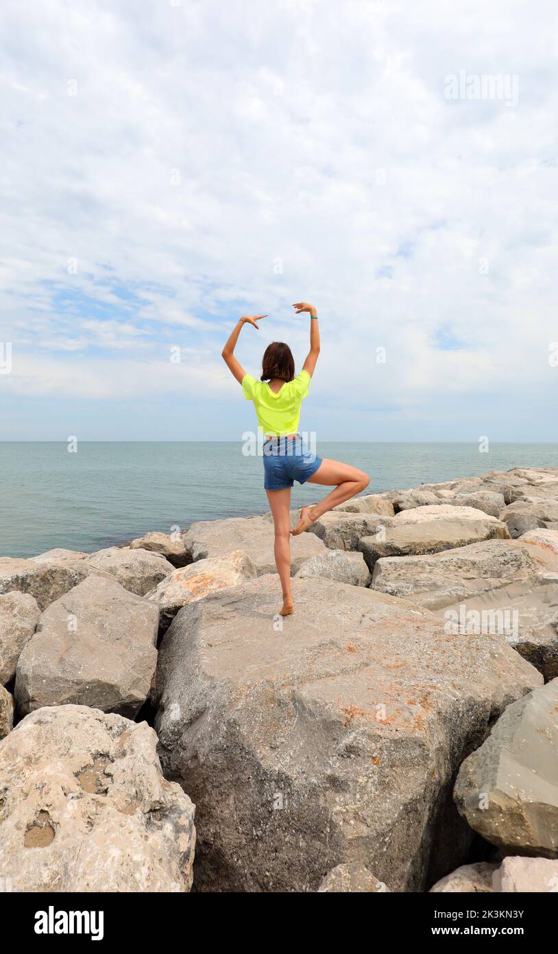 niña realiza ejercicios de gimnasia sobre las rocas junto al mar sin mostrar su cara en verano Foto de stock