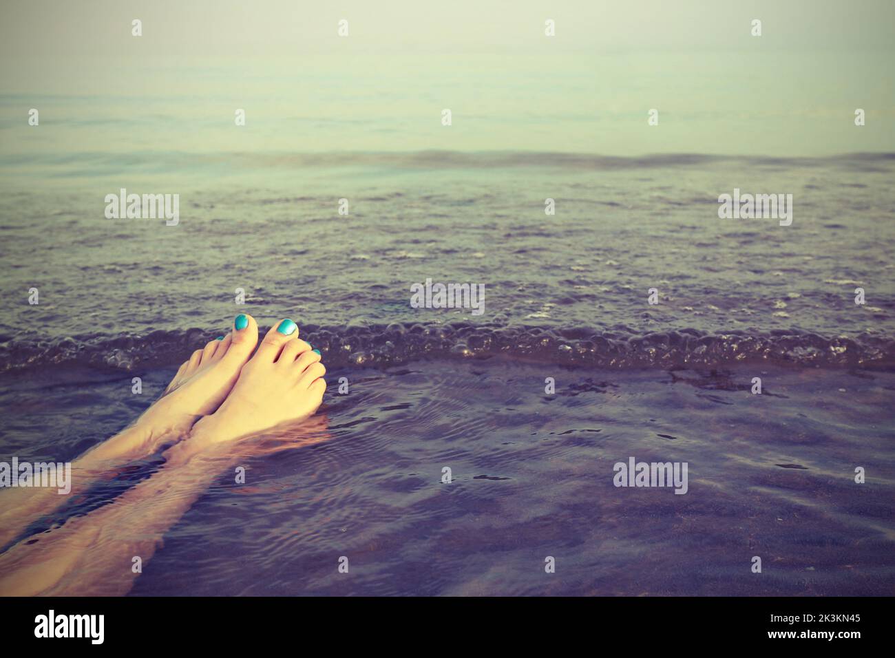 pies con uñas esmaltadas de la chica en el mar y un efecto vintage en el verano Foto de stock