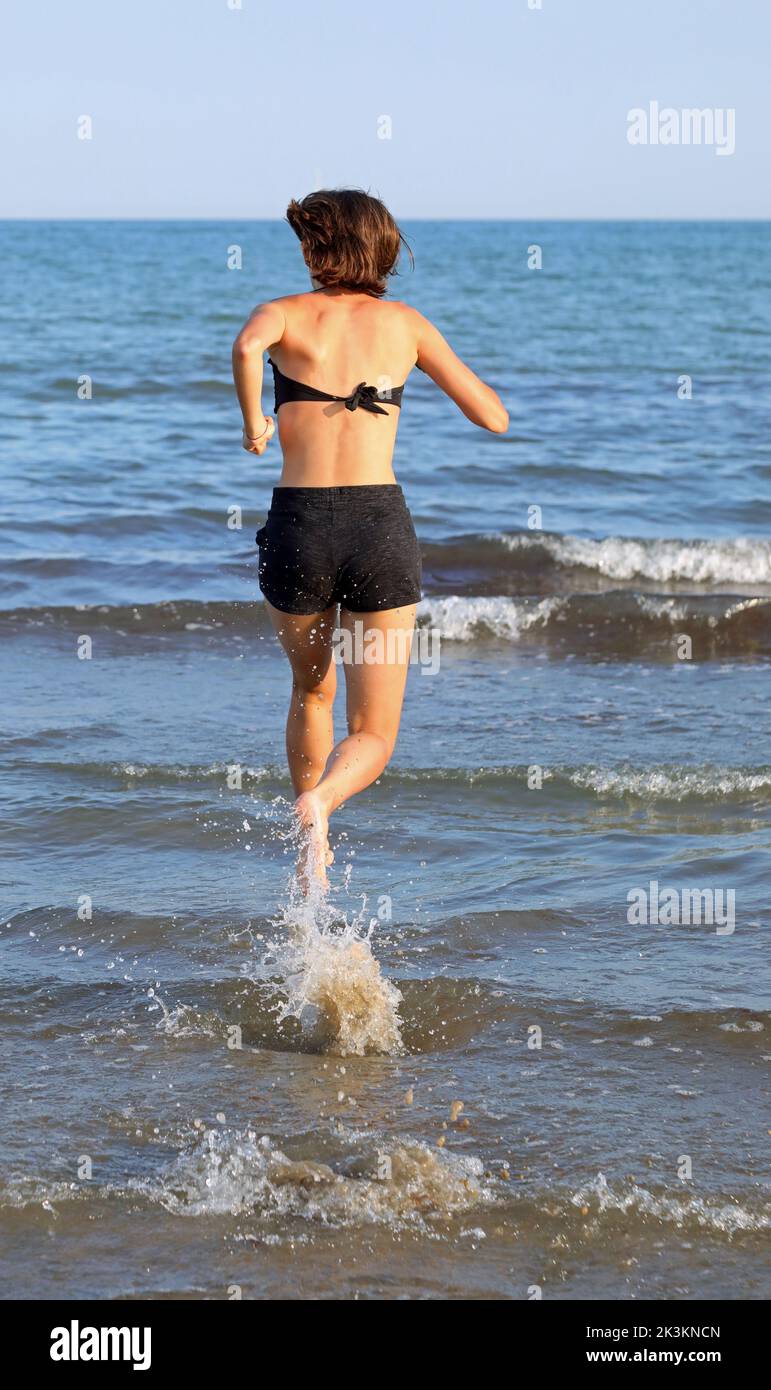 joven chica esbelta corre cerca del mar en verano para mantenerse en forma Foto de stock