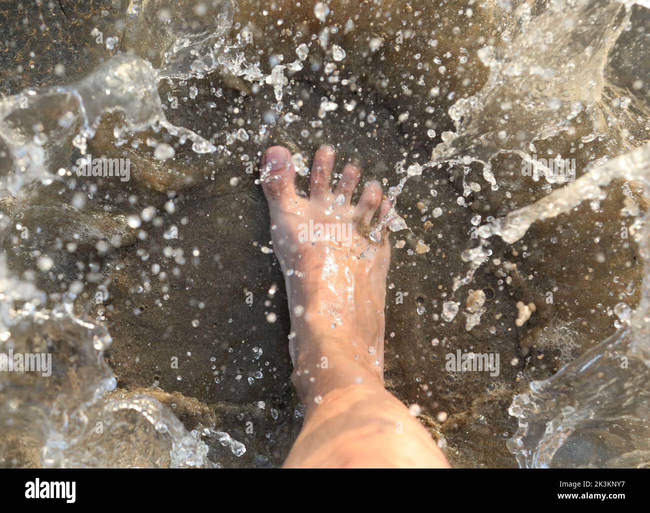 salpicaduras de agua de mar y el pie de la persona que lo pisó Foto de stock
