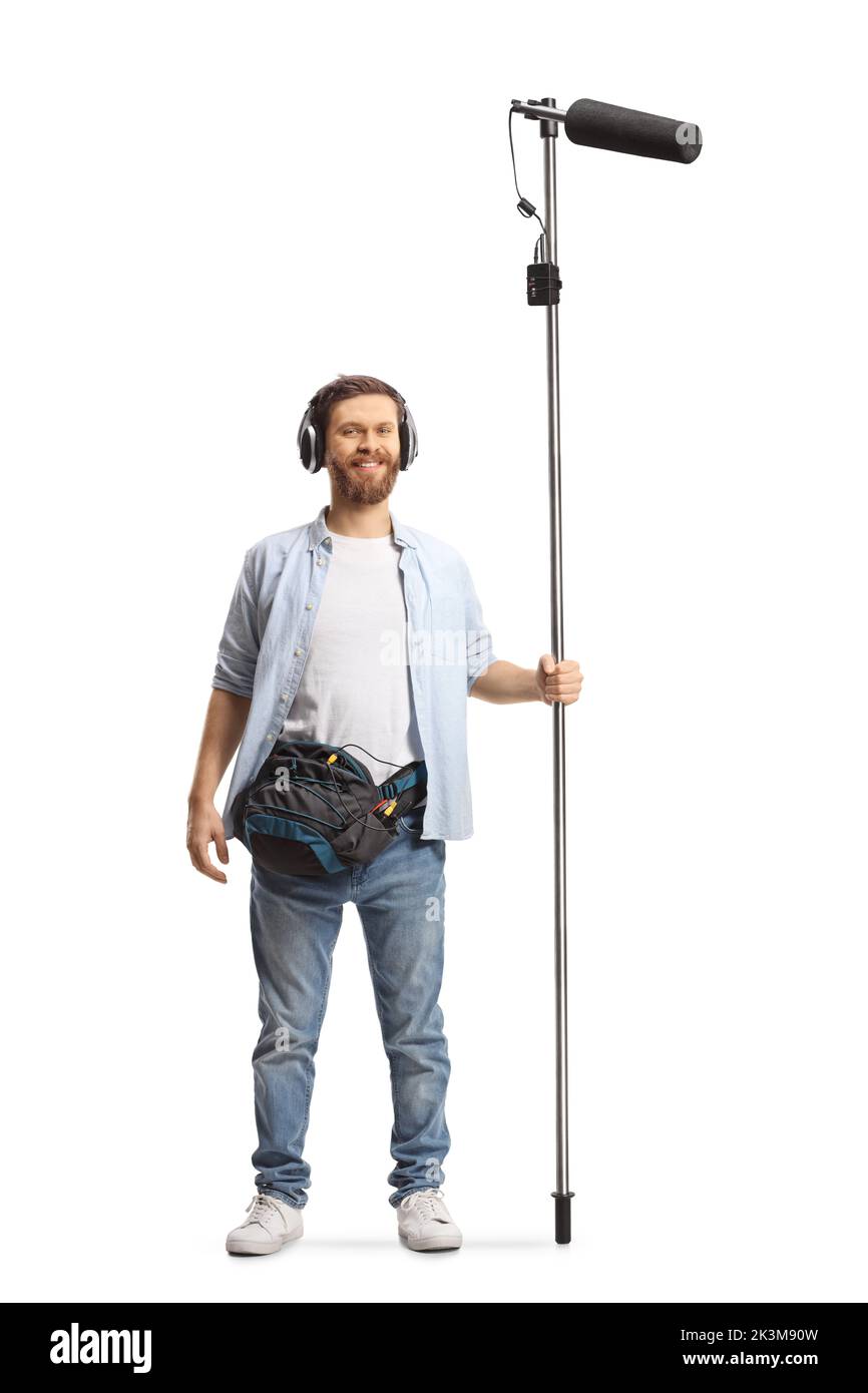 Retrato completo de un ingeniero de sonido sosteniendo un micrófono en un palo y sonriendo aislado sobre fondo blanco Foto de stock