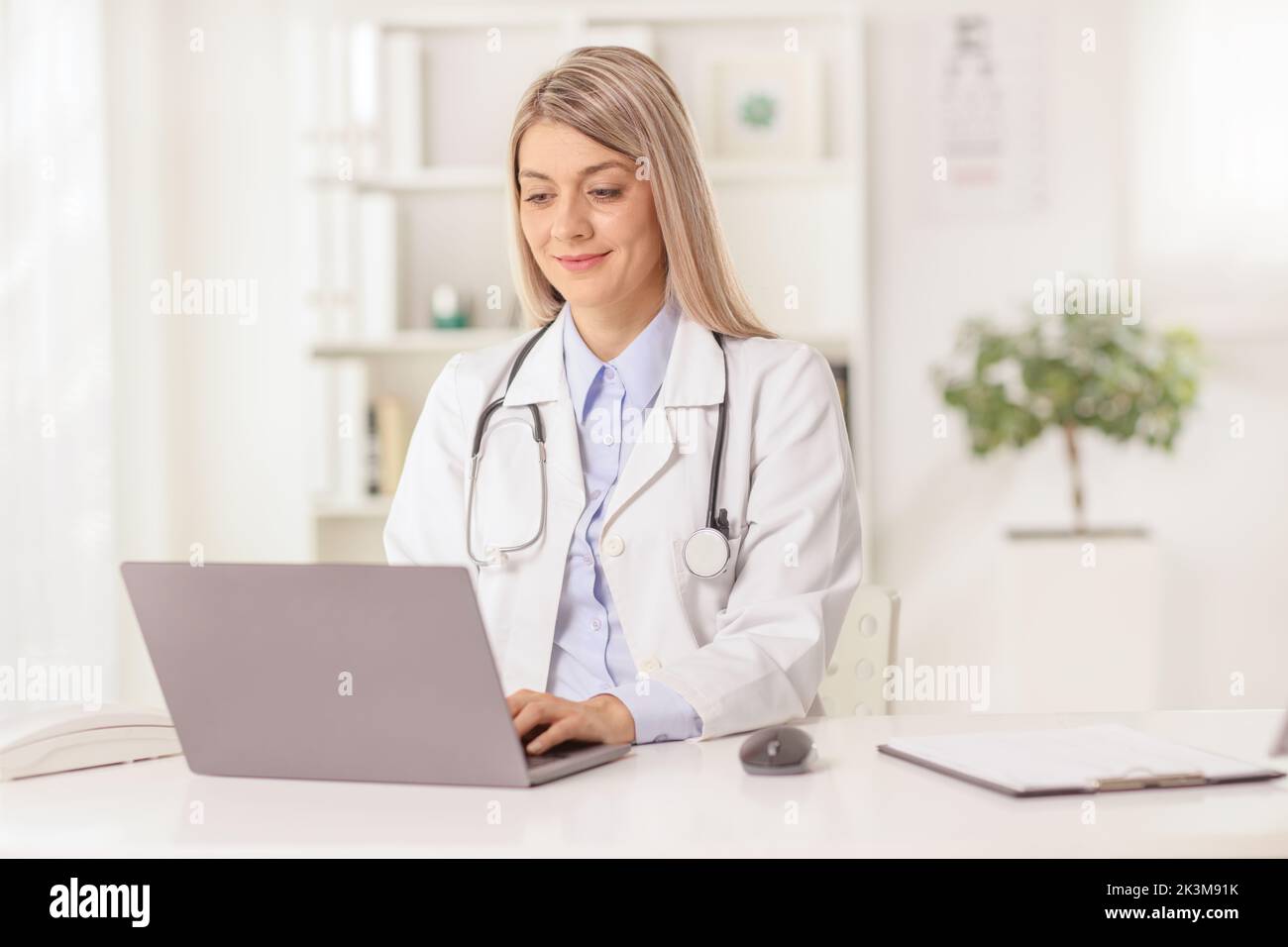 Doctora joven sentada en un consultorio y escribiendo en una computadora portátil Foto de stock