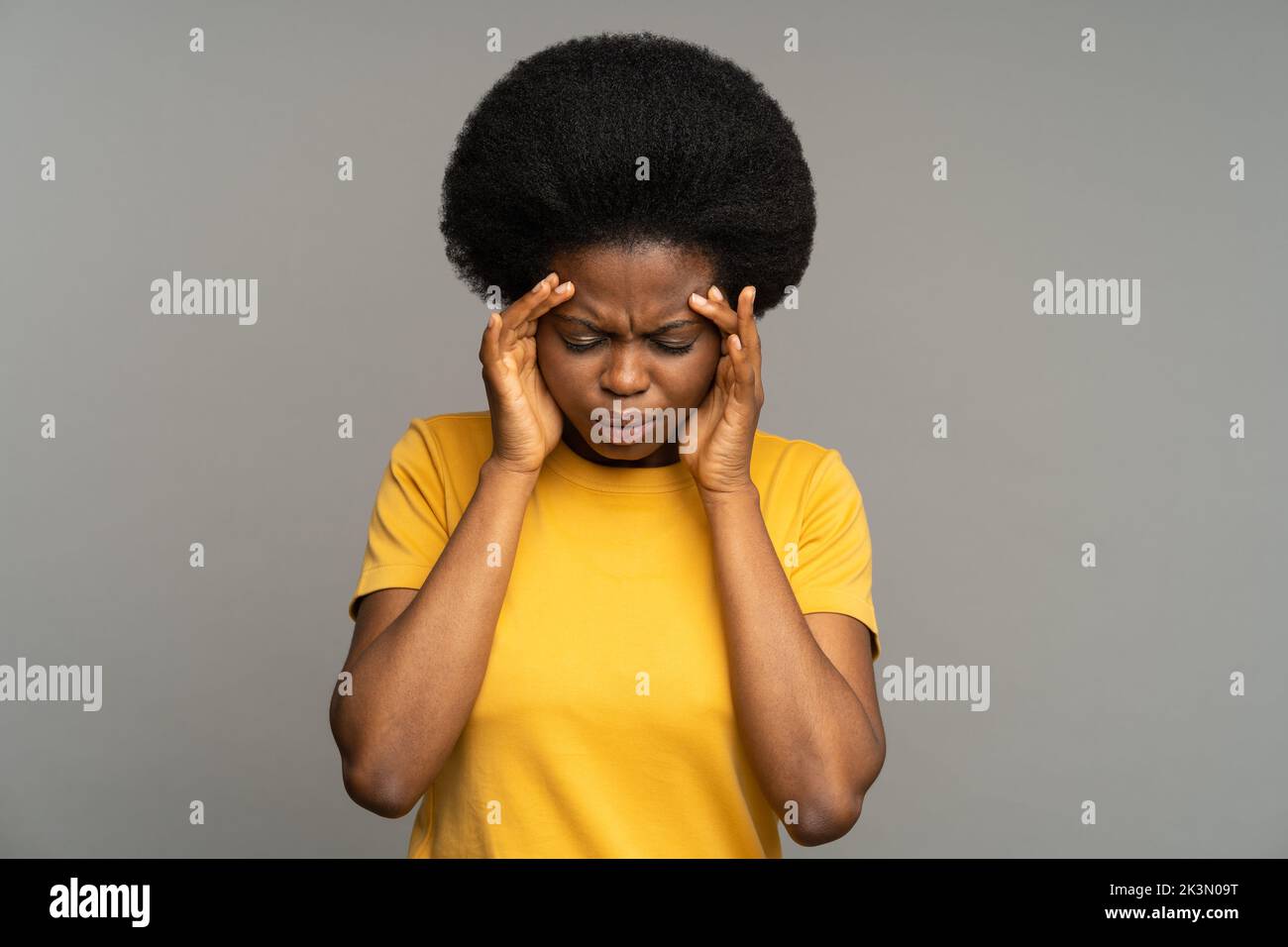 Mujer negra disgustada con cabello rizado sufre de tensión nerviosa y estrés, tocando su frente. Foto de stock