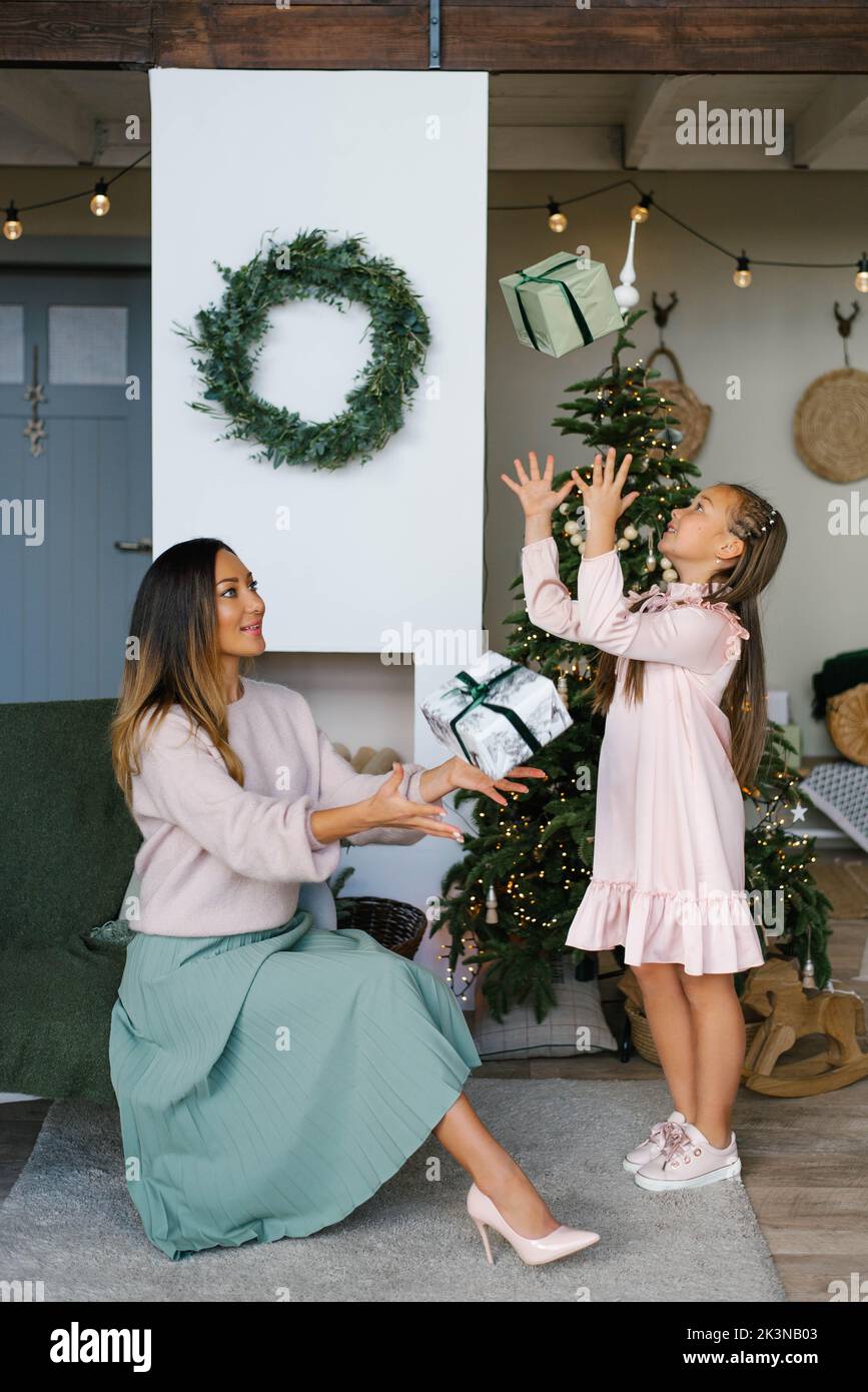 Mamá e hija en el árbol de Navidad, lanzando cajas de regalo Foto de stock