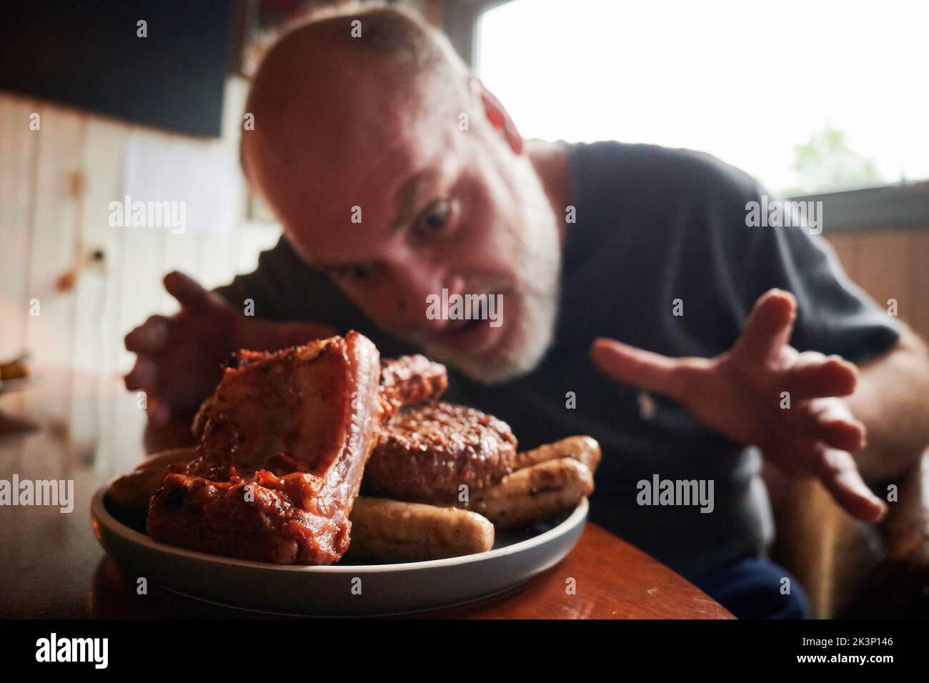Un primer plano de un plato lleno de barbacoas y un hombre que mira muy emocionado a comerlo Foto de stock