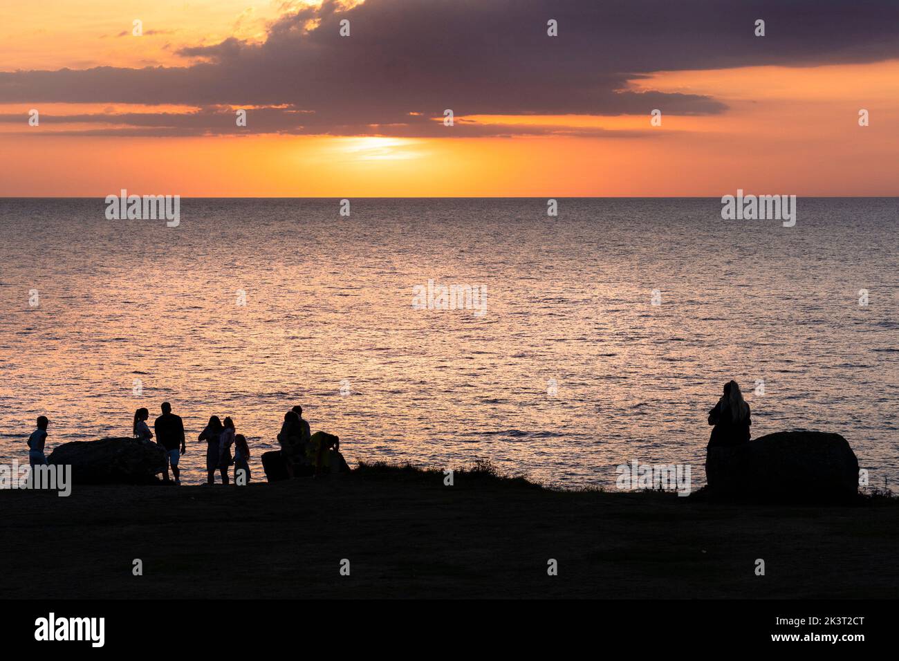 Gente de pie en la costa perfilada por una impresionante puesta de sol sobre Fistral Bay im Newquay en Cornwall en el Reino Unido en Europa Foto de stock